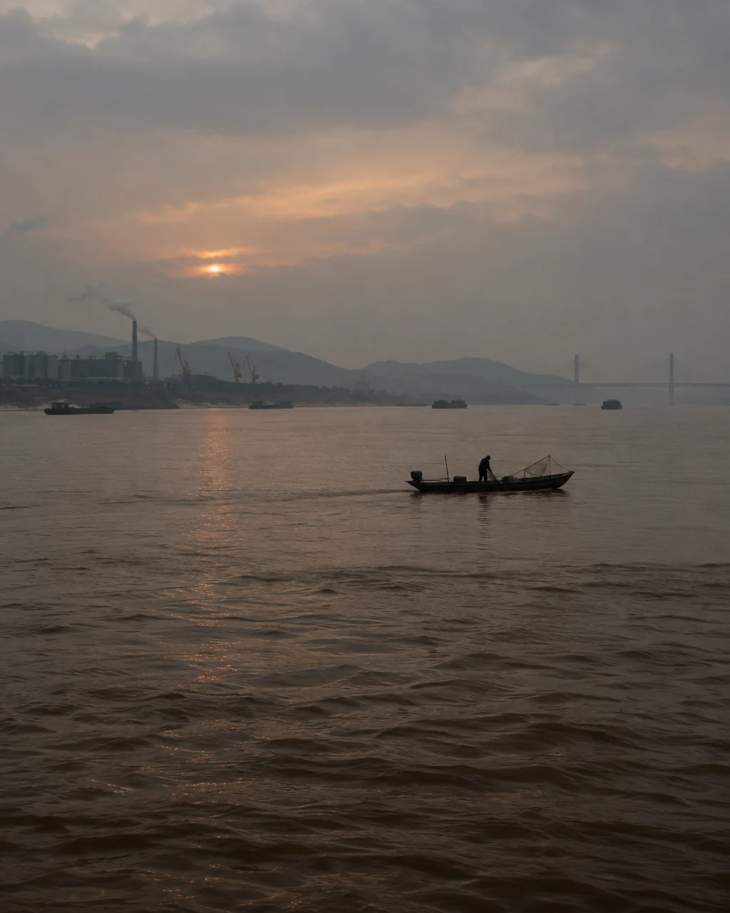 El río Yangtsé, ancho y de aguas marrones, al atardecer, con un bote pesquero pequeño en la distancia y orillas industriales
