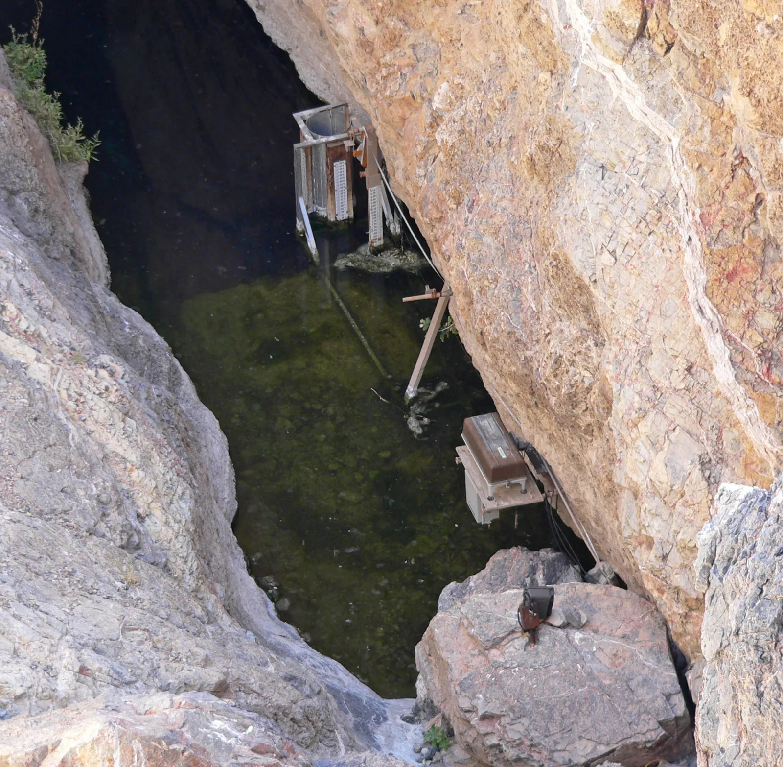La poza verde de Devils Hole vista desde arriba, al fondo de una grieta de roca, con equipos de medición junto al agua