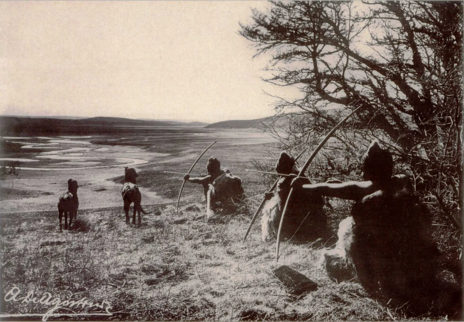 Fotografía antigua de cazadores selk'nam con arco, agachados entre arbustos frente a un valle con guanacos